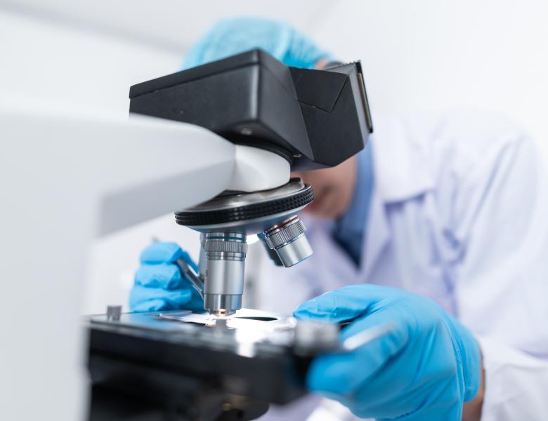 scientist in lab suit fiddling with slide in microscope